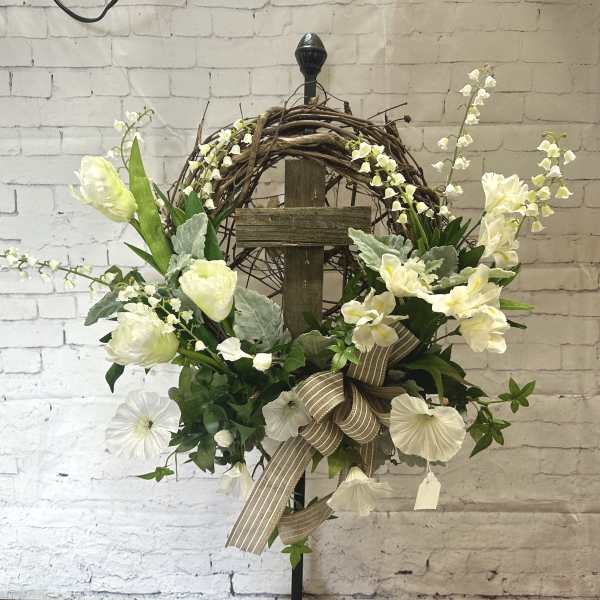 White floral wreath on a wooden cross with a striped ribbon