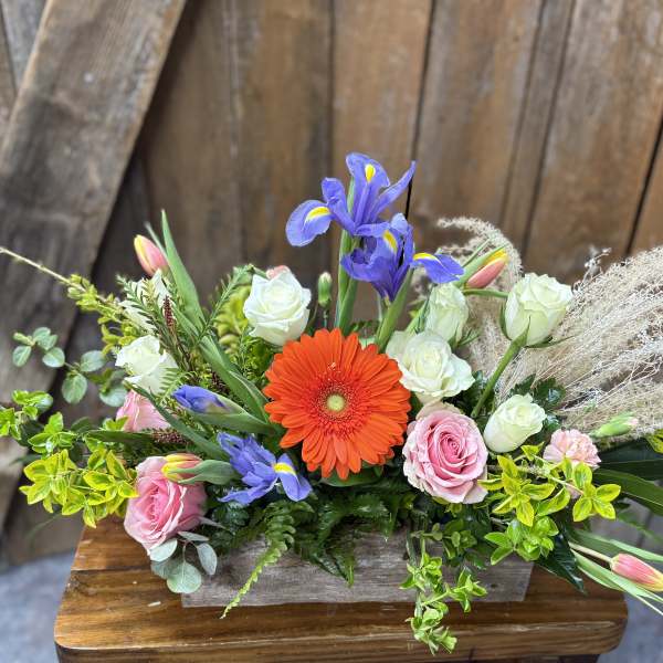 Mixed bouquet with orange gerbera, pink and white roses, and purple irises in a wooden box