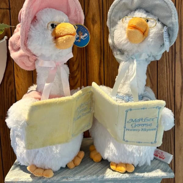 Two plush duck toys holding books, one pink and one gray