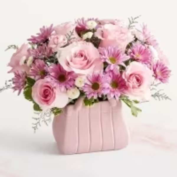 Pink roses and daisy-like blooms arranged in a pink purse-shaped ceramic vase