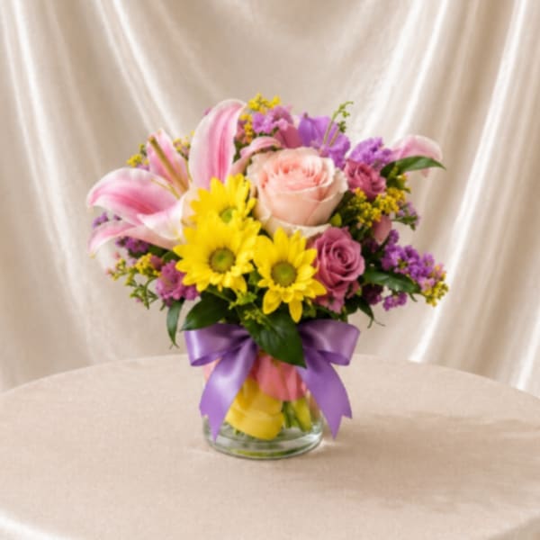 Mixed bouquet in a glass vase with pink lilies, roses, and yellow daisies
