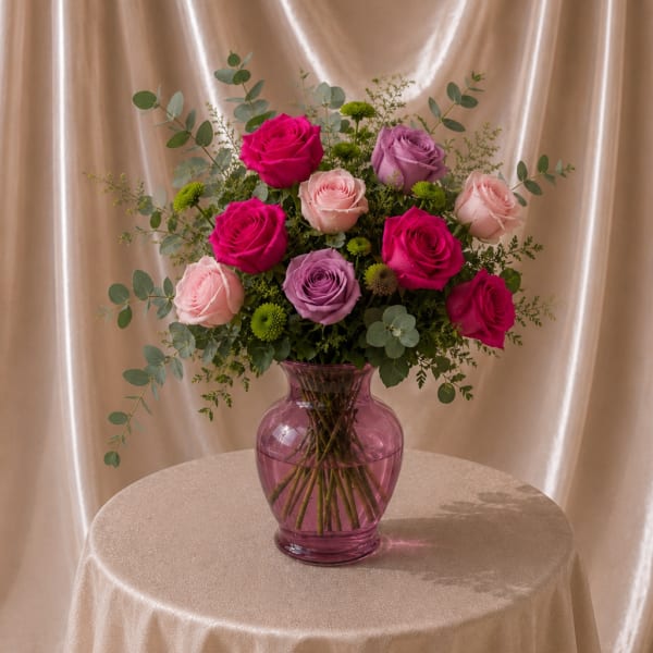 Pink and lavender roses arranged in a purple glass vase