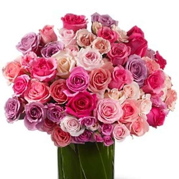 Arrangement of pink, white, and lavender roses in a clear cylinder vase wrapped with green leaves