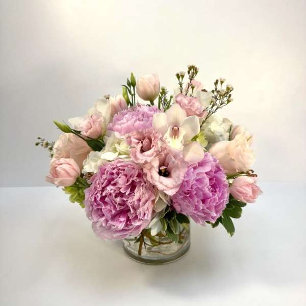 Low pink and white arrangement with peonies, tulips, and lisianthus in a clear glass vase