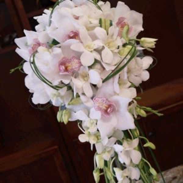 Cascading bridal bouquet of white orchids with pink centers displayed in a clear glass vase
