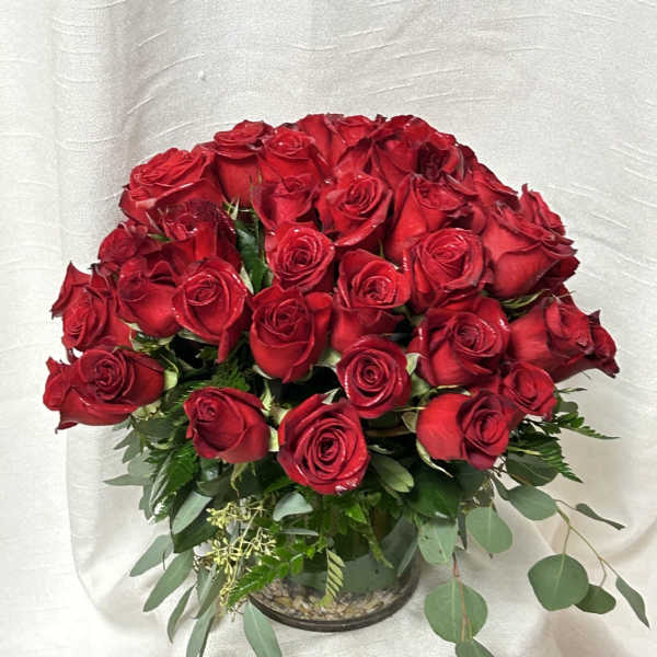 Bouquet of red roses in a glass vase with mixed greenery