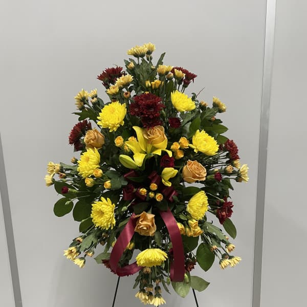 Standing floral spray with yellow and burgundy flowers on an easel