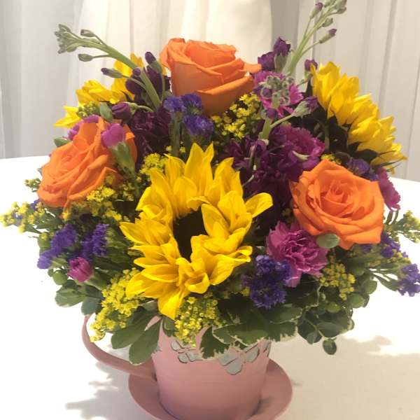 Bouquet of orange roses and yellow sunflowers in a pink mug-style vase