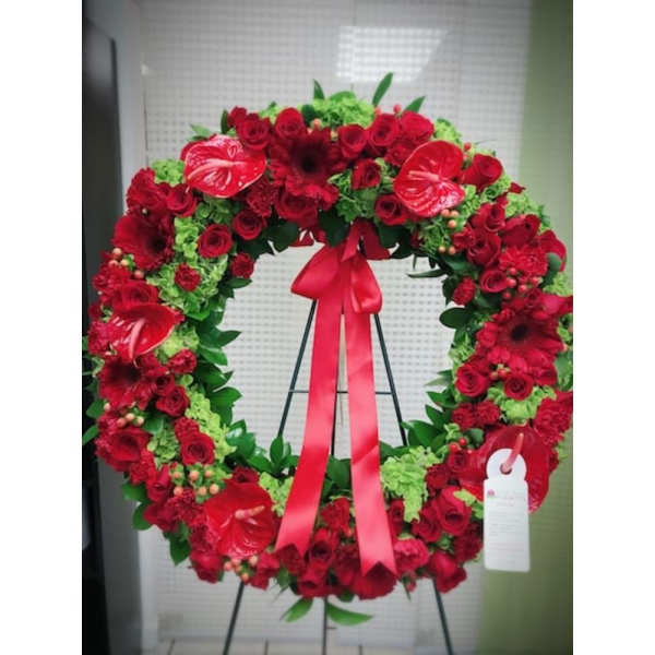 Large standing wreath of red flowers and green accents with a red ribbon bow on an easel.