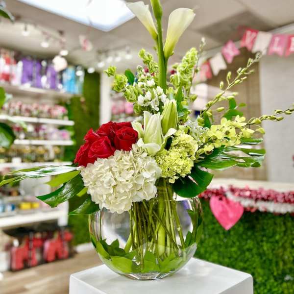 Low glass bowl of red roses, white hydrangeas, calla lilies and green blooms in an asymmetrical arrangement