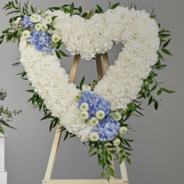 Heart-shaped white floral wreath with blue accents on a wooden easel