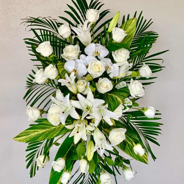 White roses and lilies arranged with palm leaves on a standing easel