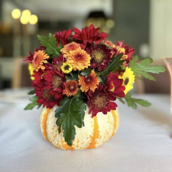 Fall bouquet of red and orange flowers in a small pumpkin vase