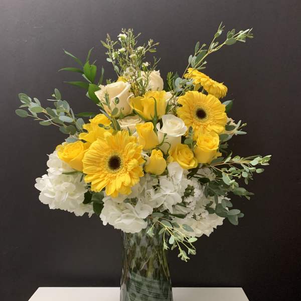 Yellow gerbera daisies and white roses in a glass vase
