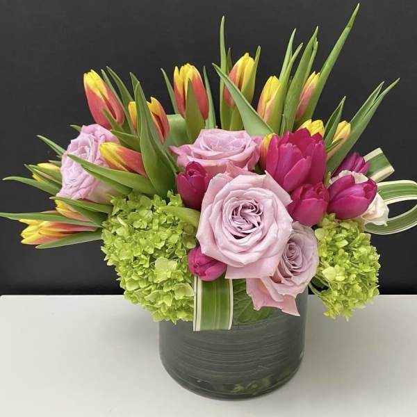Low glass vase arrangement of pink roses, tulips, and green hydrangeas.
