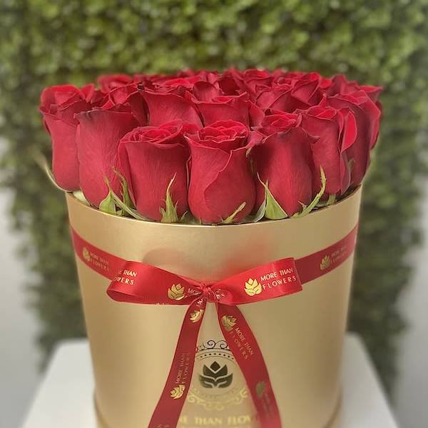 Round box of tightly packed red roses in a gold hatbox with a red ribbon bow