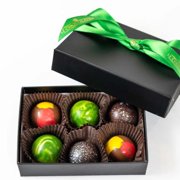 Black gift box of six colorful round chocolates with a green ribbon on the lid