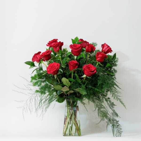 Red roses arranged in a clear glass vase with airy greenery