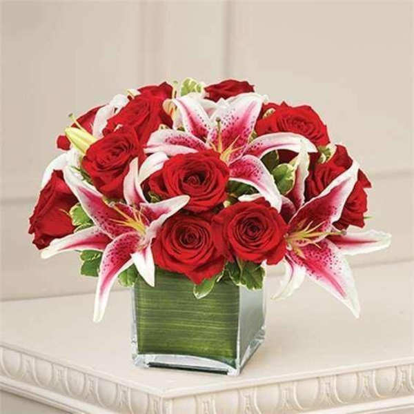 Red roses and pink lilies arranged in a square glass vase