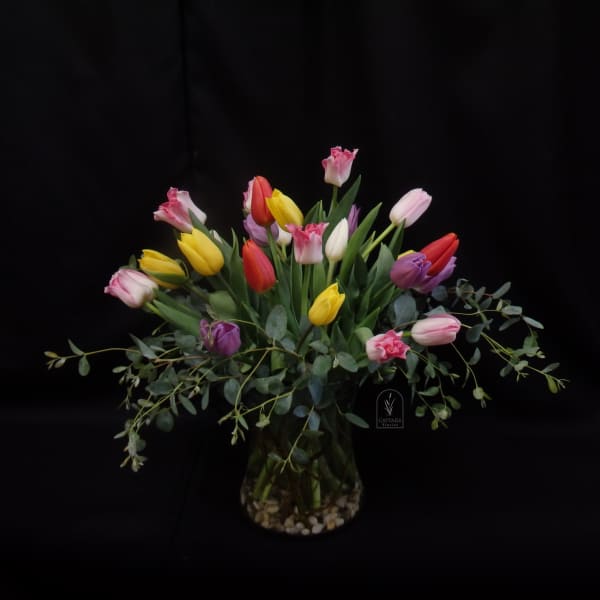 Mixed tulips in a glass vase with trailing greenery