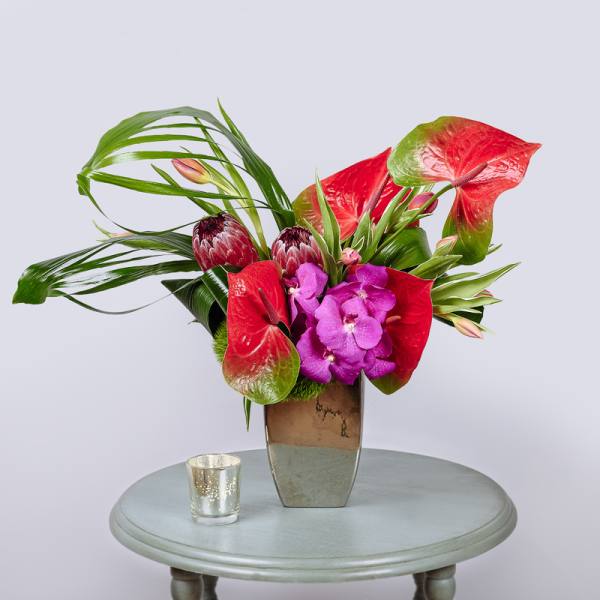 Tropical flower arrangement in a tall vase with red anthuriums and purple orchids