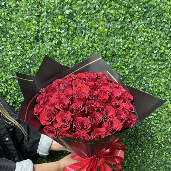 Large bouquet of red roses wrapped in black paper with a red ribbon