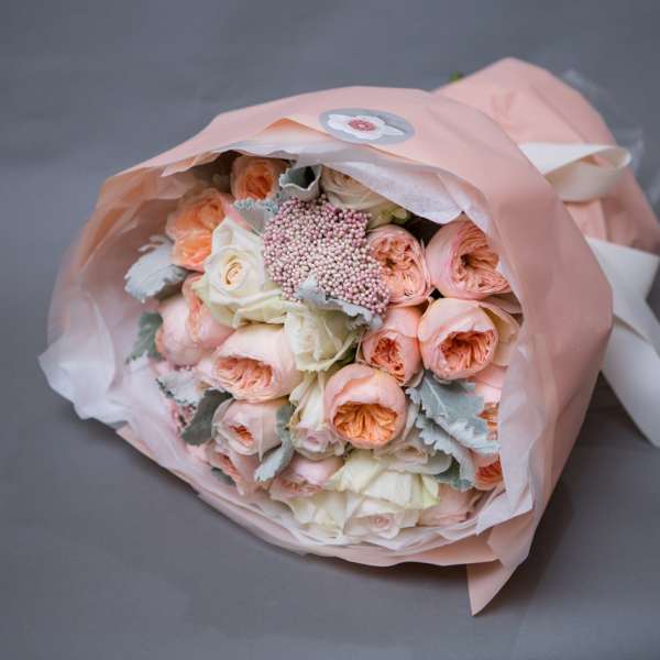 Bouquet of peach and white roses wrapped in pink paper