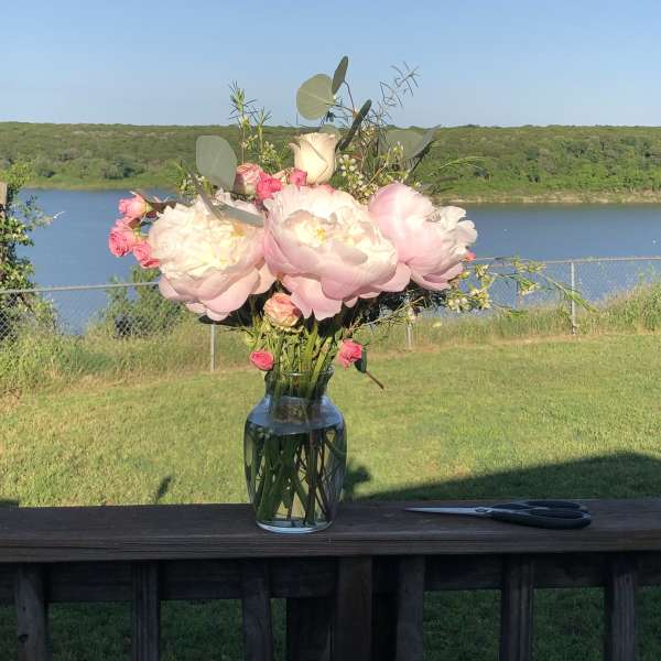 Pink and white peonies with small roses in a glass vase