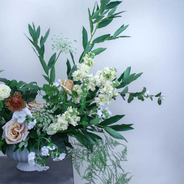 White and blush flowers in a white pedestal vase with tall greenery