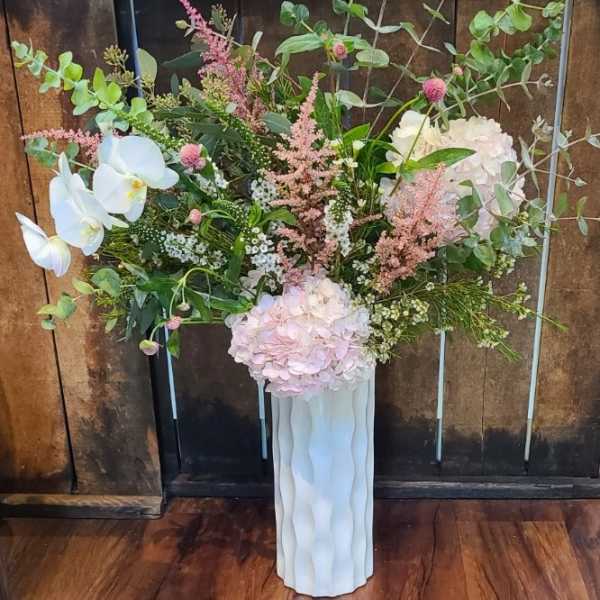 Tall floral arrangement with pale pink hydrangeas and white orchids in a white vase