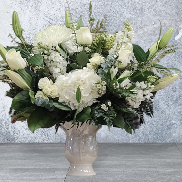 White floral arrangement in a beige vase with lilies, roses, and hydrangeas