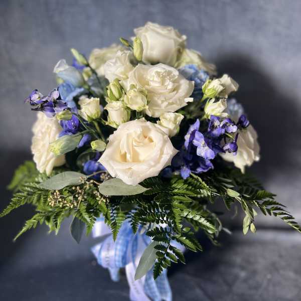 White roses and blue flowers in a hand-tied bouquet with ribbon