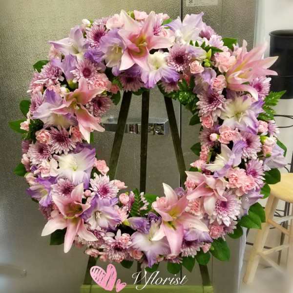 Pink and lavender wreath of lilies, carnations, and mums displayed on a wooden easel