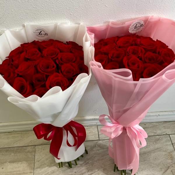 Two bouquets of red roses wrapped in white and pink paper with ribbons