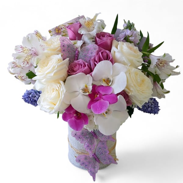 White and pink roses and orchids with lavender accents in a cylinder vase with decorative butterflies.