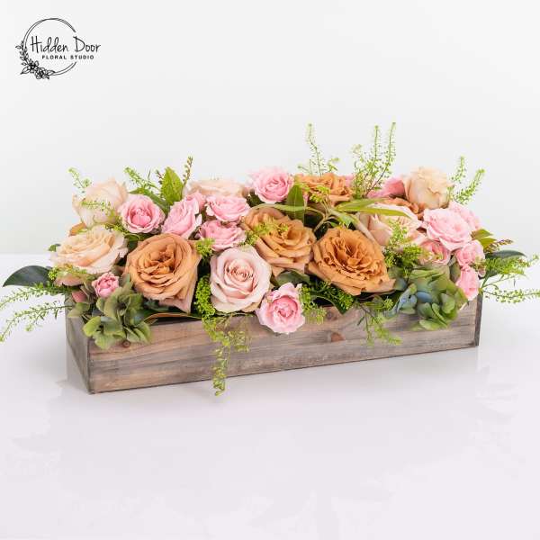 Low floral arrangement of pink and peach roses in a wooden box