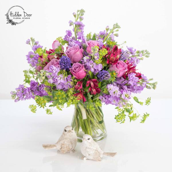 Bouquet of pink and purple flowers in a glass vase with two bird figurines