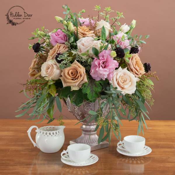 Mixed rose arrangement in a silver urn with teacups on a table
