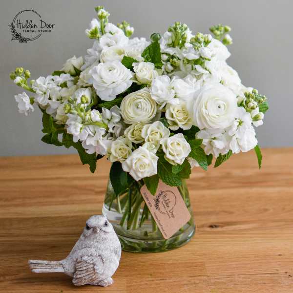 White flowers arranged in a glass vase with a small bird figurine in front