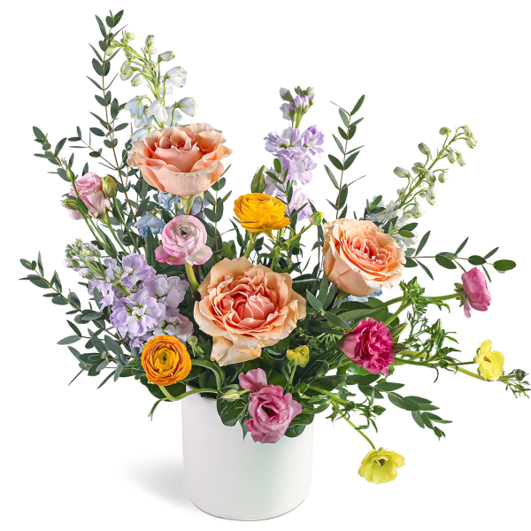 Mixed arrangement of peach roses, ranunculus, and lavender blooms in a white vase