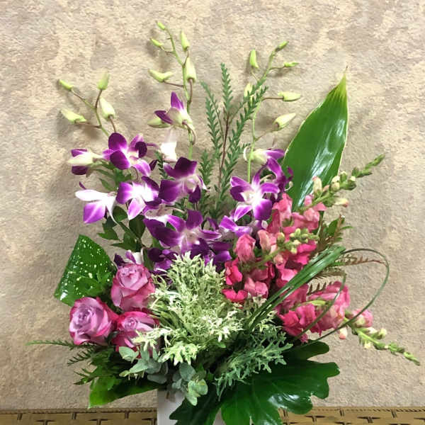 Purple orchids and pink flowers arranged in a white square vase