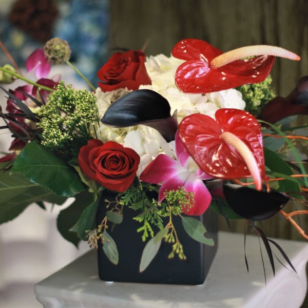 Arrangement of red roses, white hydrangeas, and red anthuriums in a black vase