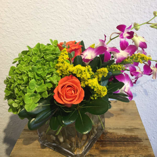 Orange rose and purple orchids in a glass vase with green hydrangea