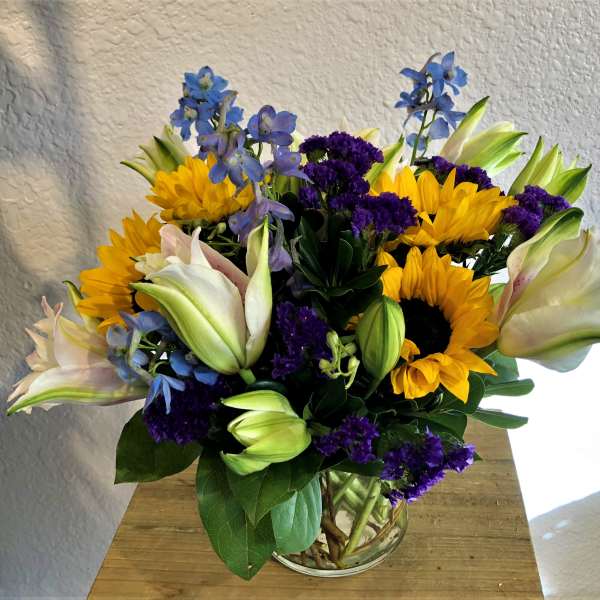 Bouquet of sunflowers, lilies, and purple flowers in a glass vase