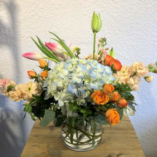 Mixed bouquet with blue hydrangea, orange roses, and pink tulips in a glass vase