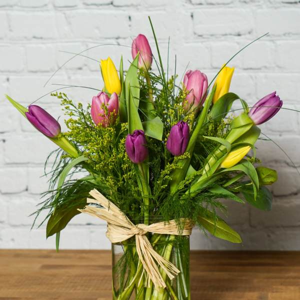 Colorful tulips arranged in a glass vase with a raffia bow