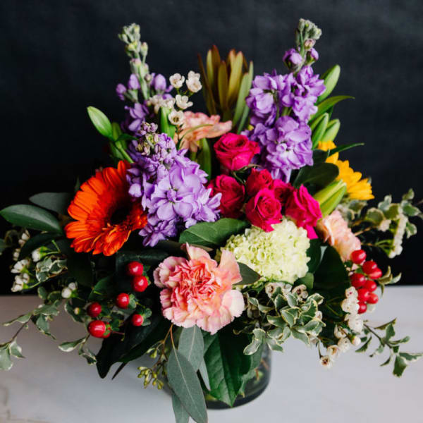 Colorful mixed bouquet in a glass vase with roses, lilies, and gerbera daisies
