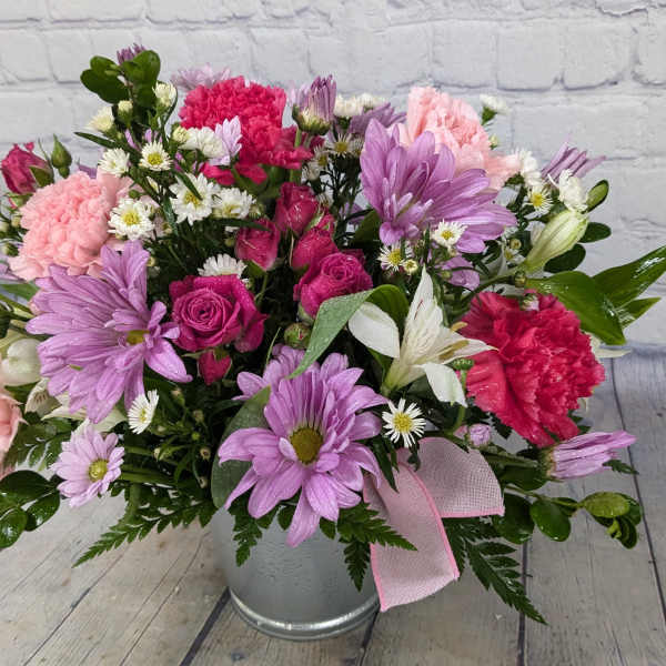 Pink and purple mixed flower arrangement in a metal bucket with a ribbon