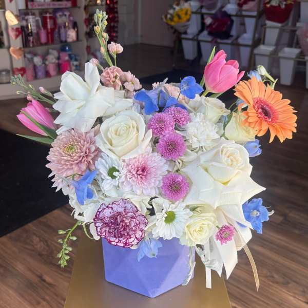 Mixed bouquet of roses, tulips, daisies, and other blooms in a purple box.