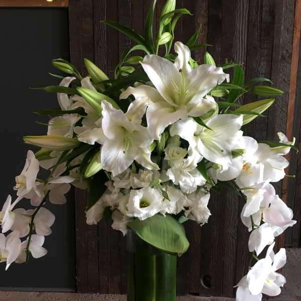 White lilies and orchids arranged in a tall glass vase